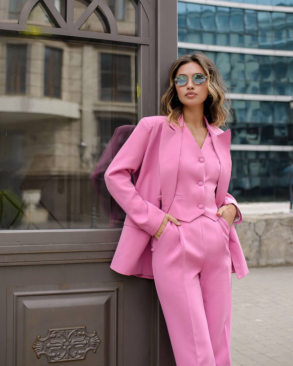 Woman in a pink suit standing against a building entrance.