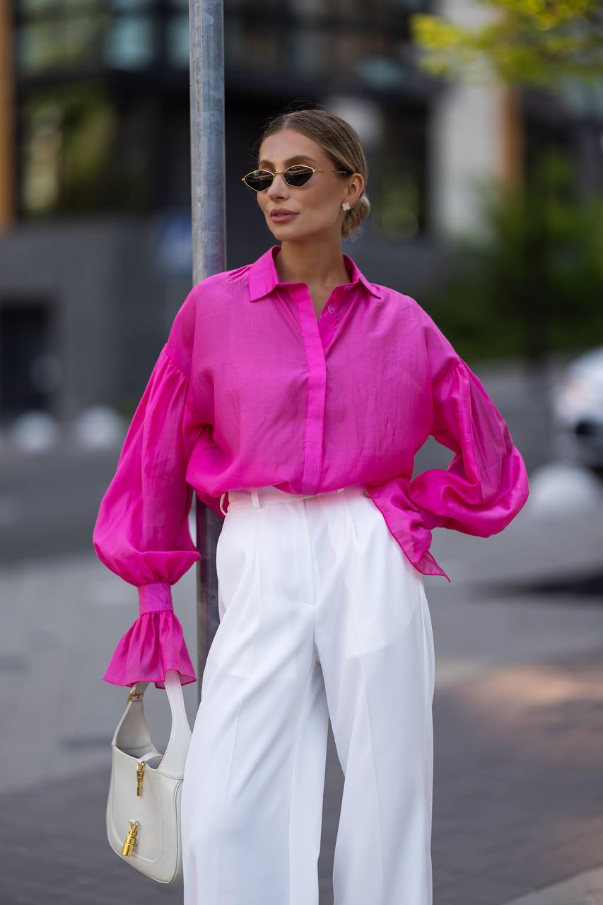 Woman wearing a bright pink shirt and white pants on a city street.