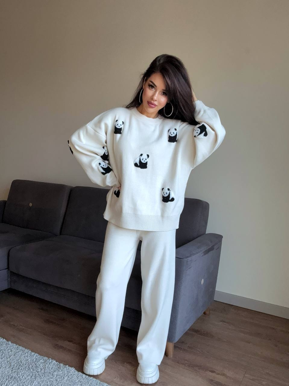 Woman wearing a white sweater with panda designs in a living room.