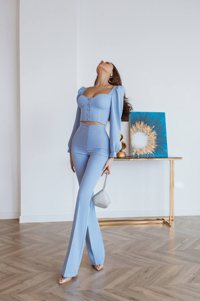 Woman in a light blue outfit standing in a room with a decorative table and artwork.