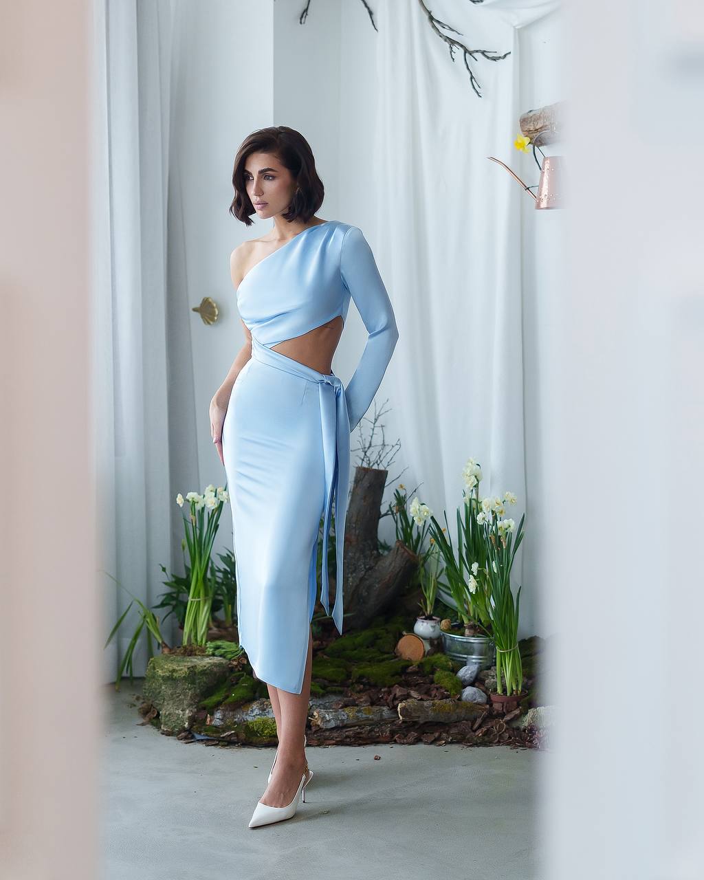 Woman in a light blue dress standing in a room with plants and decor.