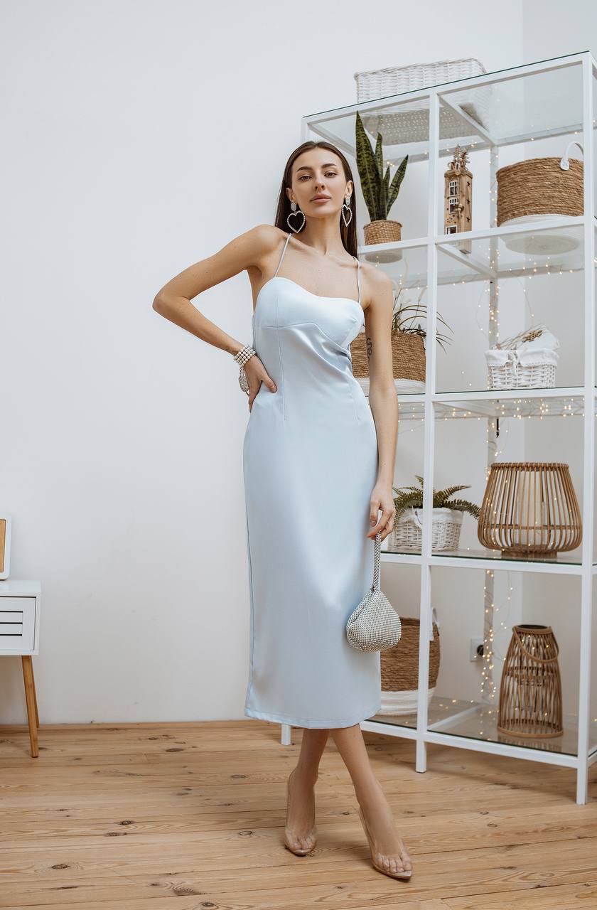 Woman in a light blue dress standing in a room with a white shelf and wooden floor.