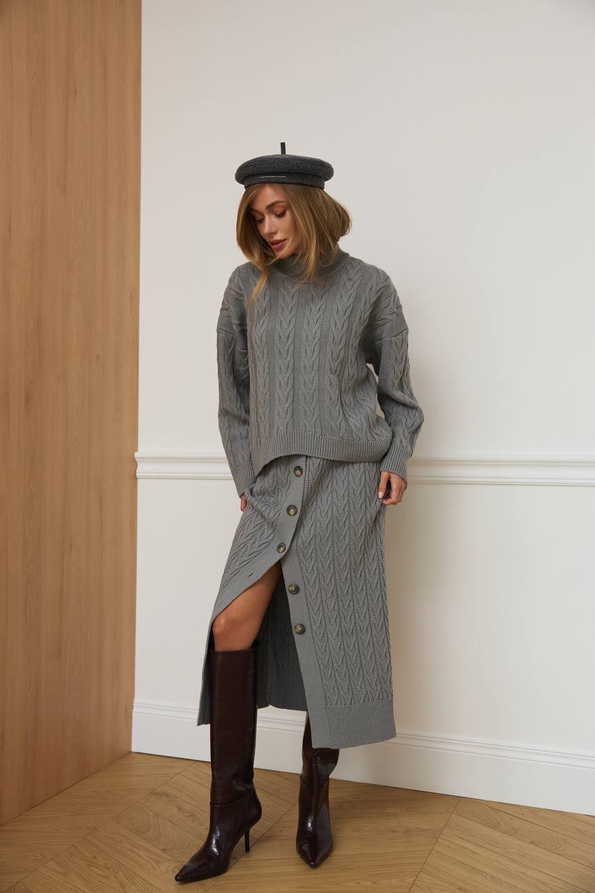 Woman wearing a gray knit outfit with a beret against a white wall.