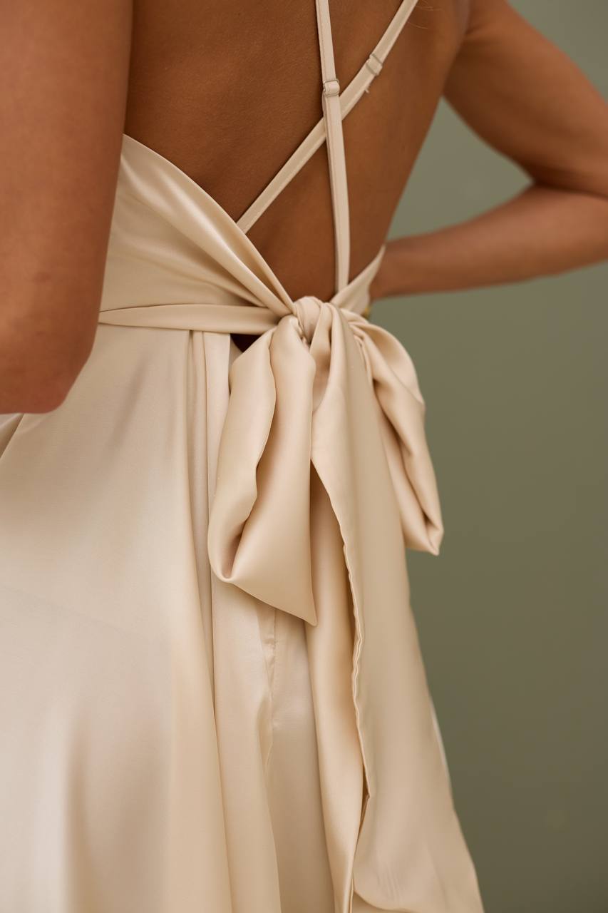 Beige dress with criss-cross straps and a bow detail on a neutral background