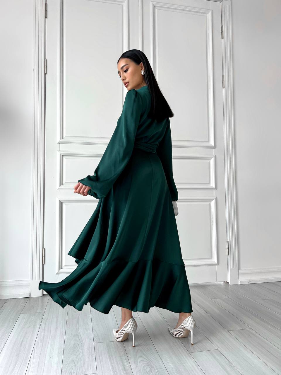 Woman in a long dark green dress standing in a room with white walls and floor.
