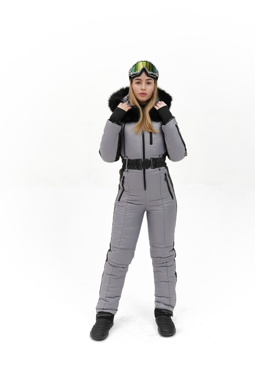 Person wearing a gray snowsuit with black boots and a helmet on a white background
