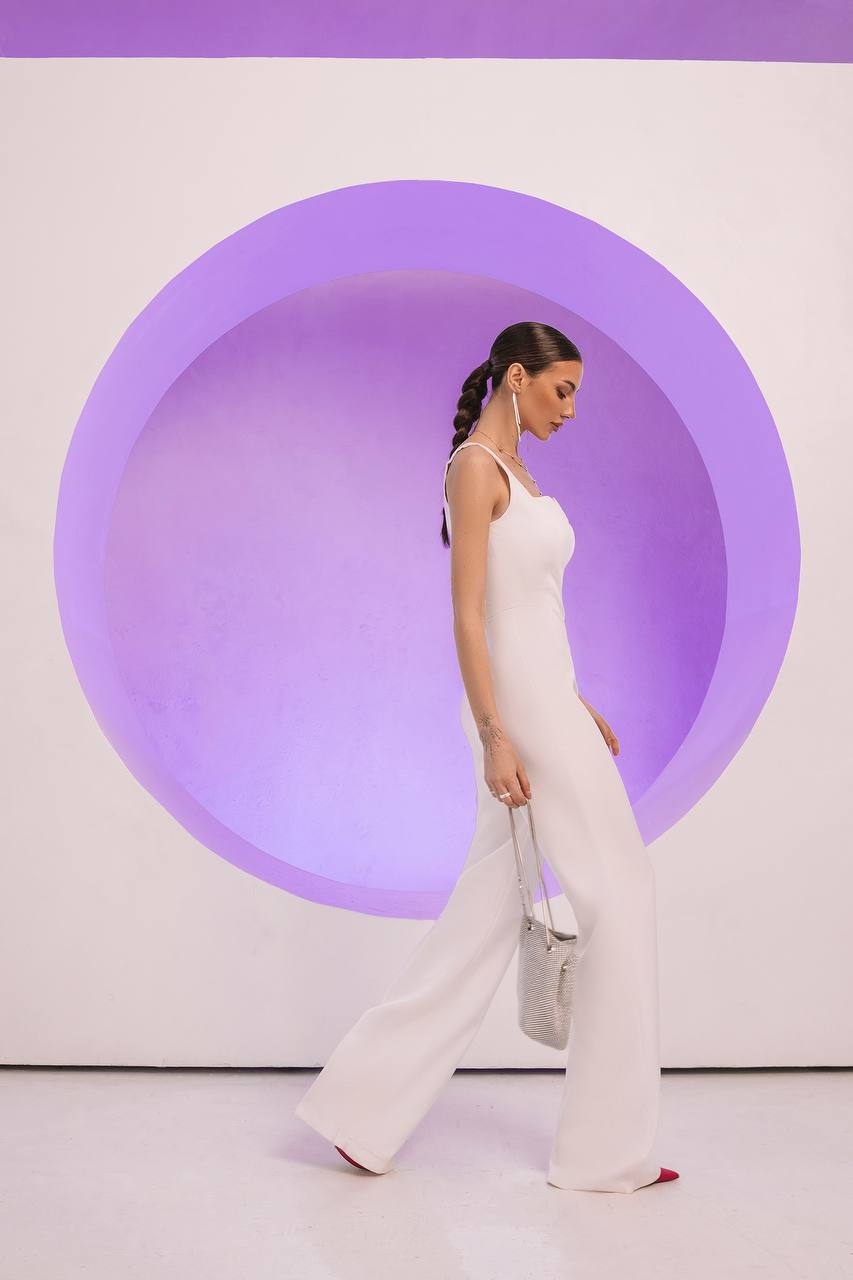Woman in a white outfit standing against a purple circular wall.