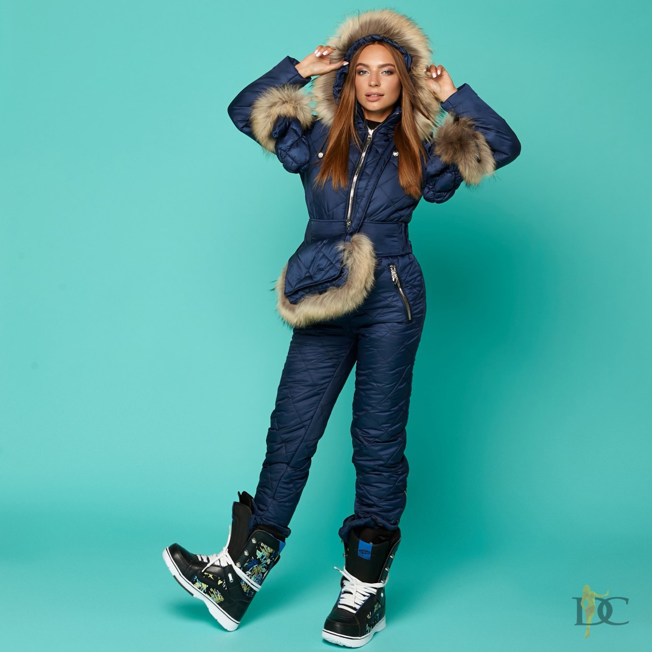 Person wearing a blue snowsuit with fur trim on a teal background