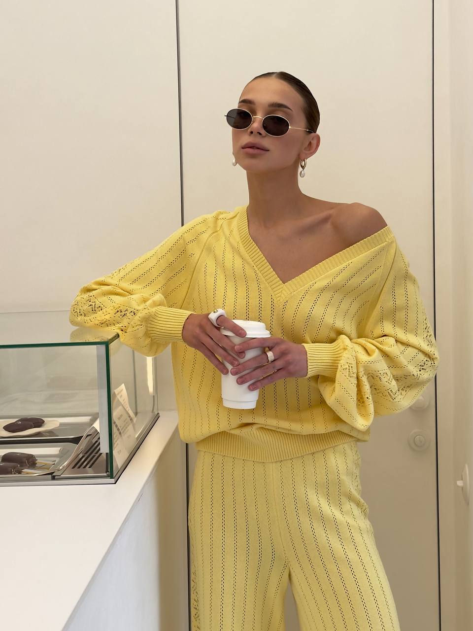 Woman wearing a yellow outfit holding a coffee cup indoors.