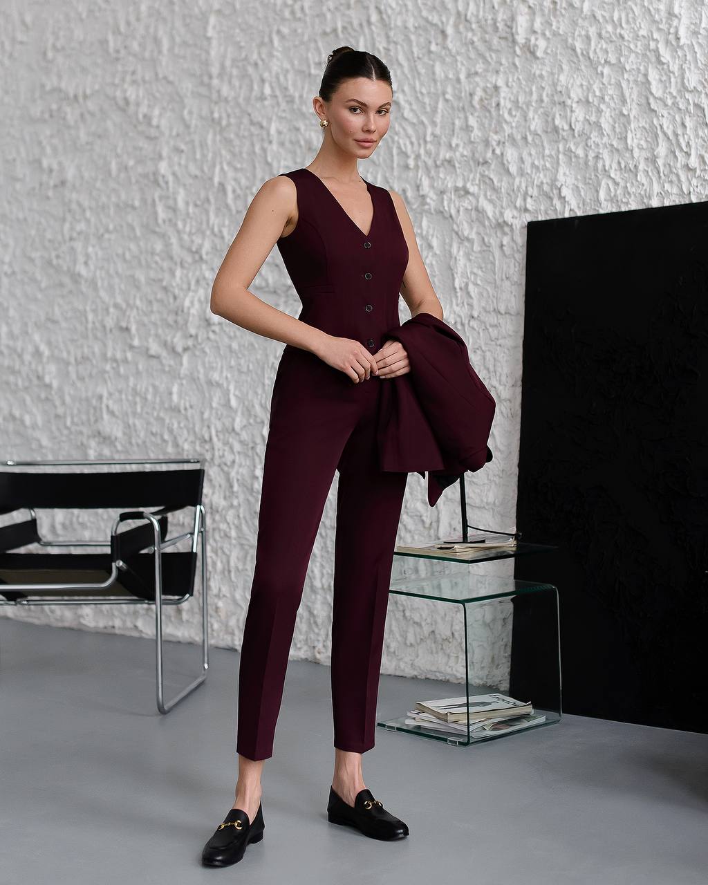 Woman in a burgundy jumpsuit standing in a minimalistic room with a textured wall.