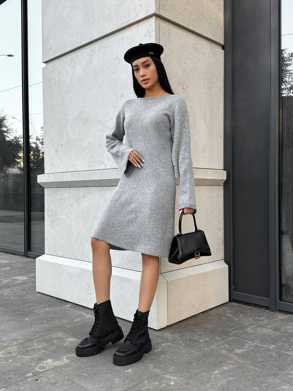 Woman in a gray dress and black boots standing against a building.