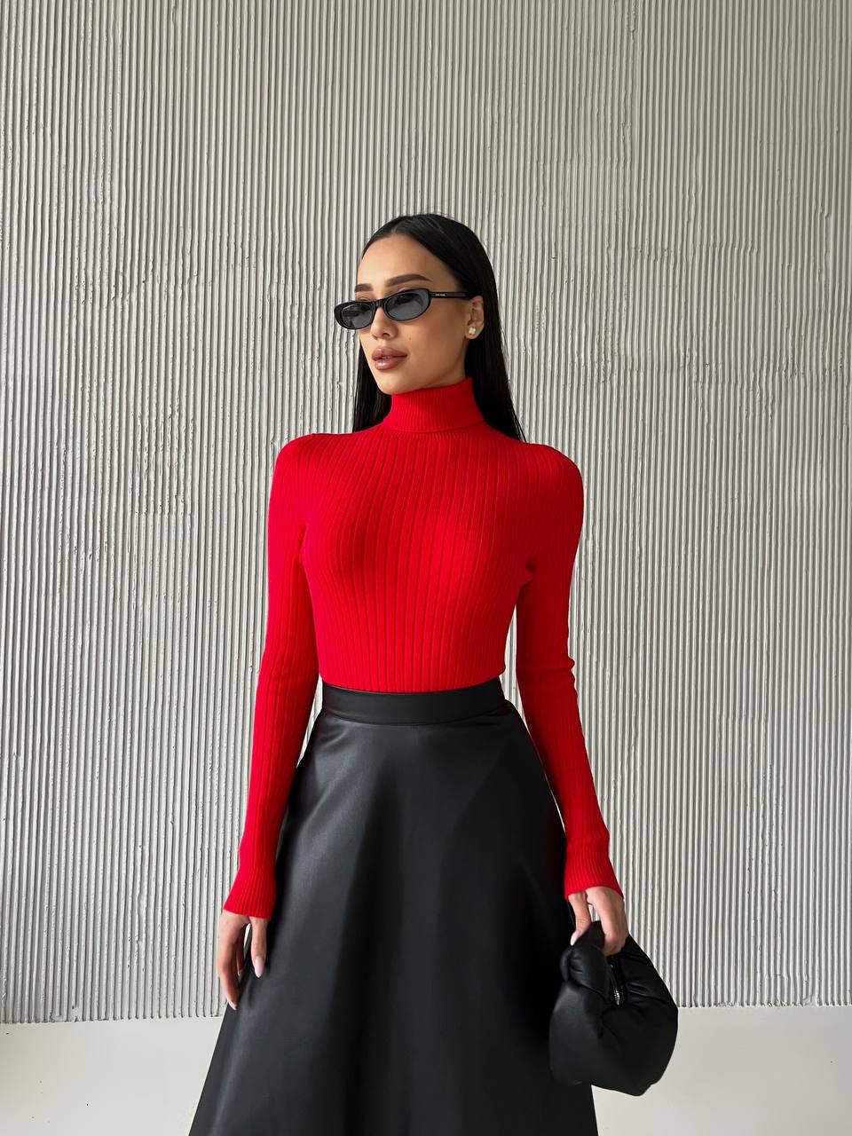 Woman wearing a red turtleneck and black skirt against a striped wall.