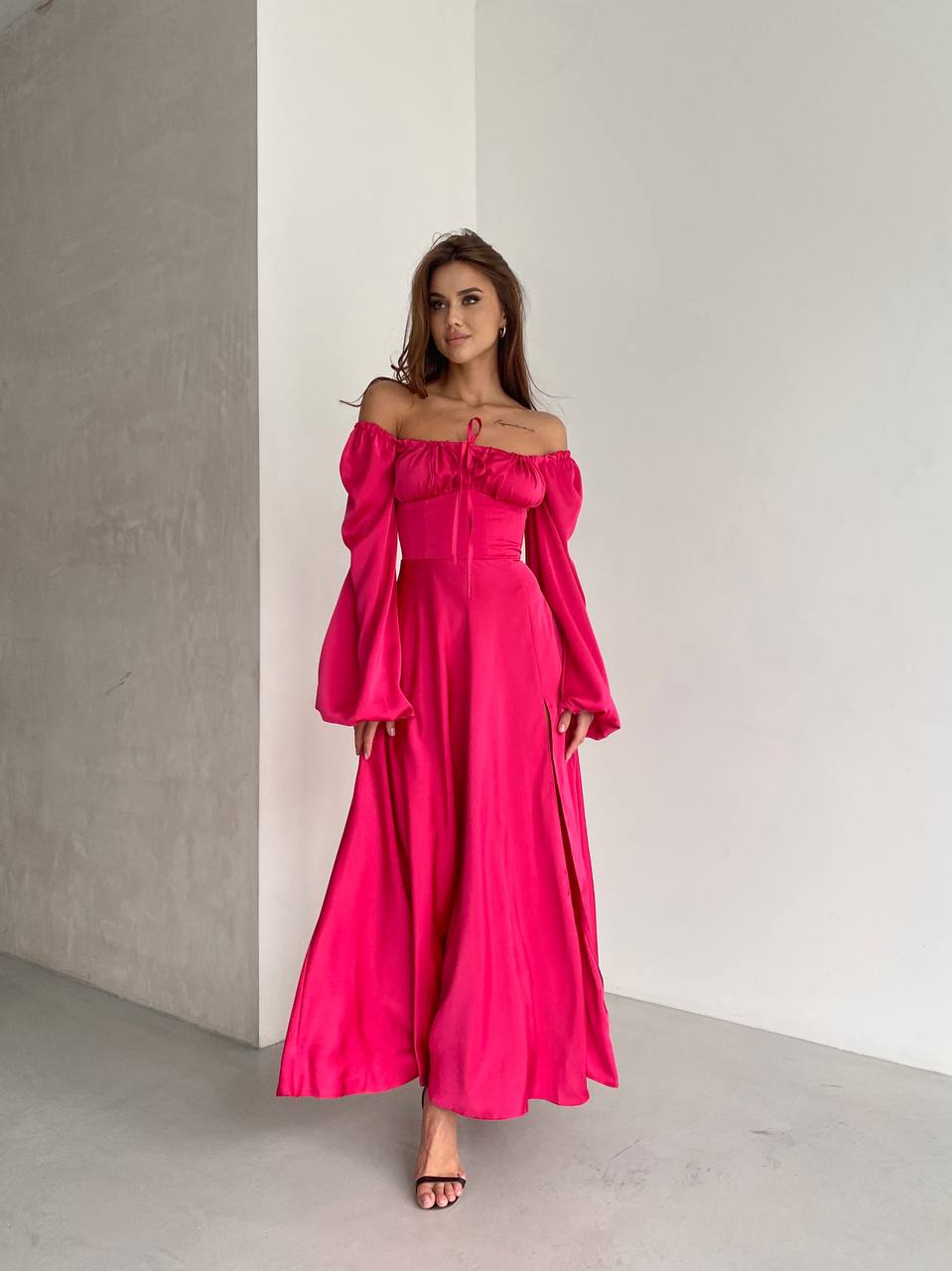 Woman wearing a bright pink off-shoulder dress against a plain background