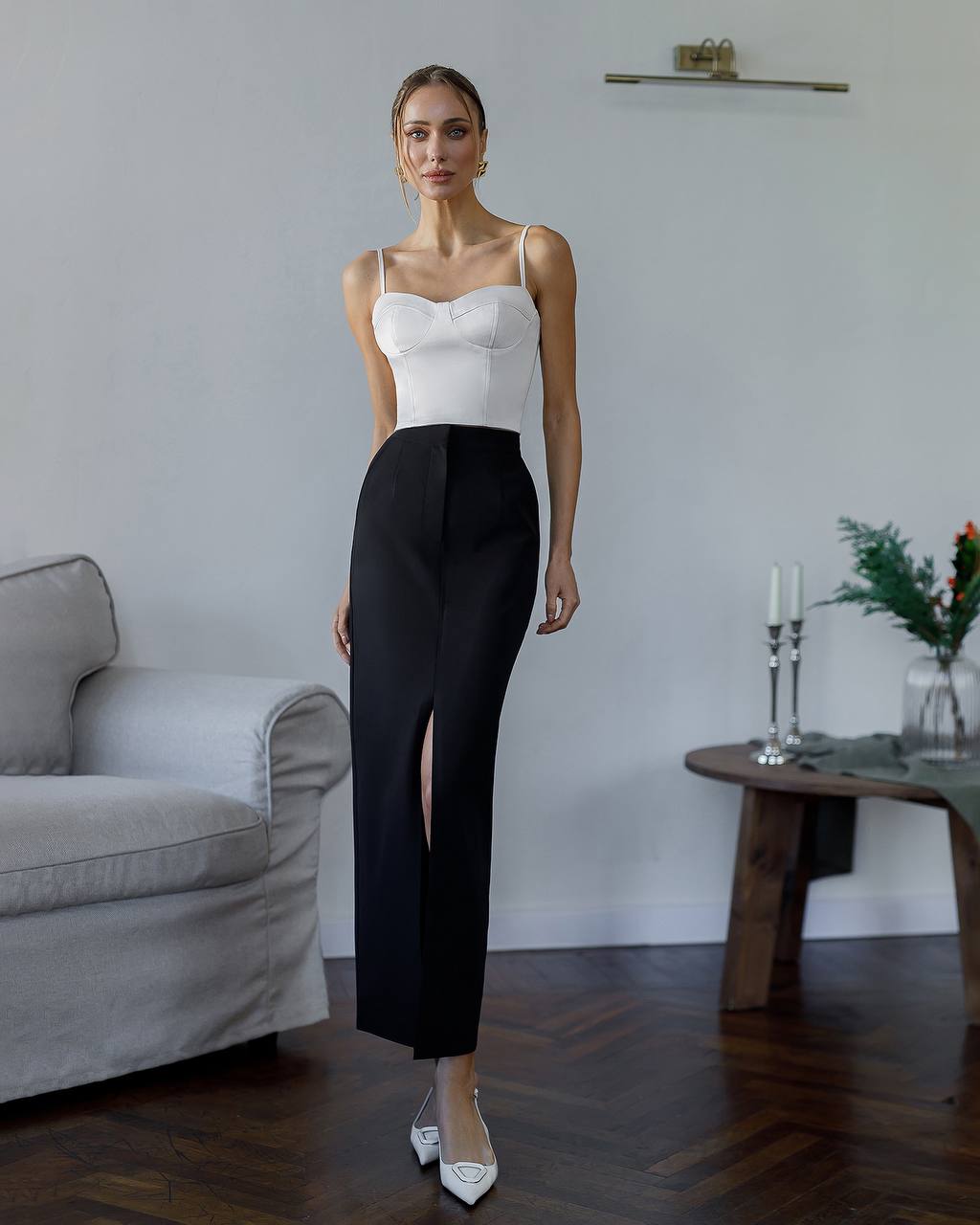 Woman in a white top and black pants standing in a living room.