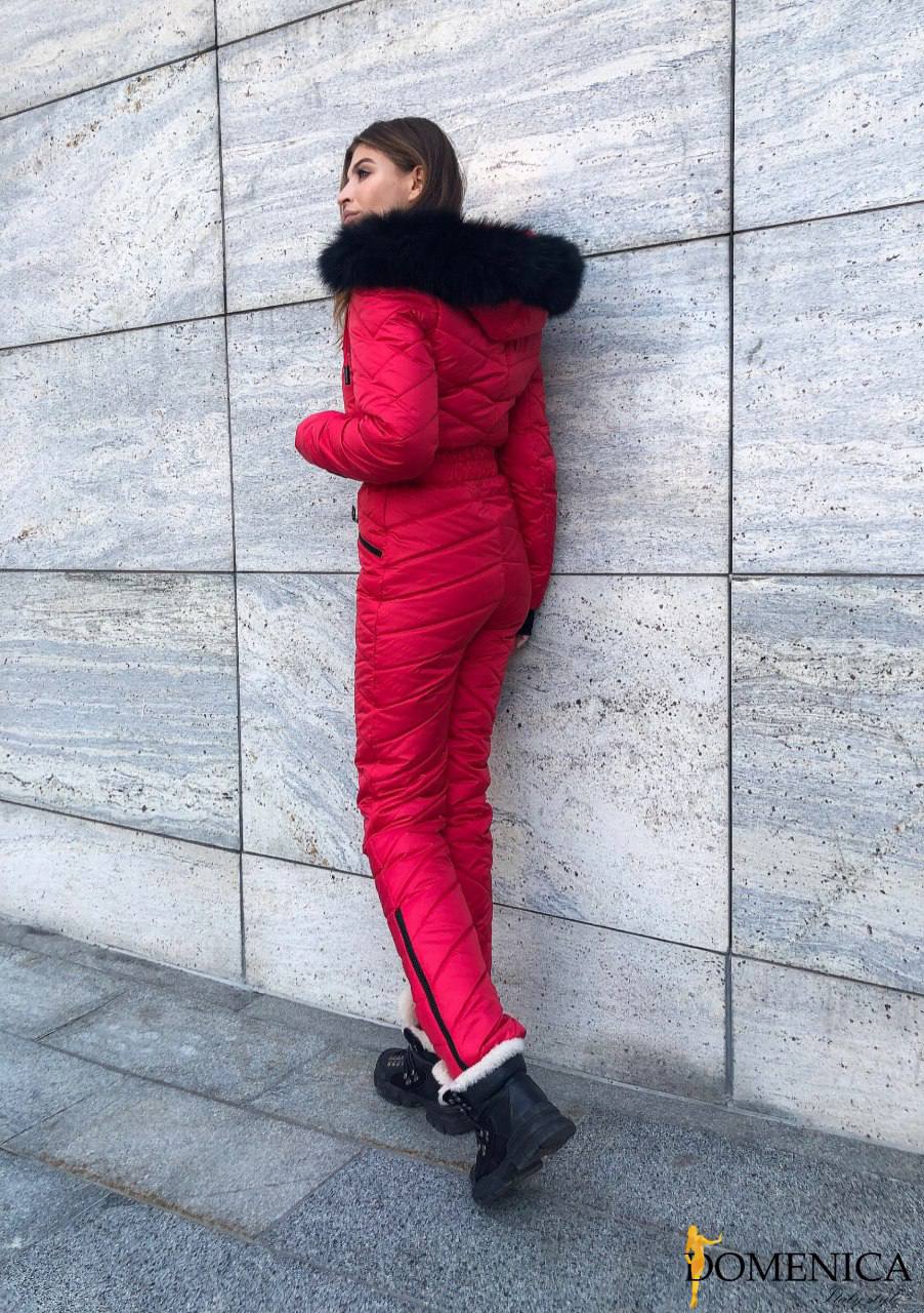 Person wearing a red puffer jumpsuit with black fur trim against a gray stone wall.
