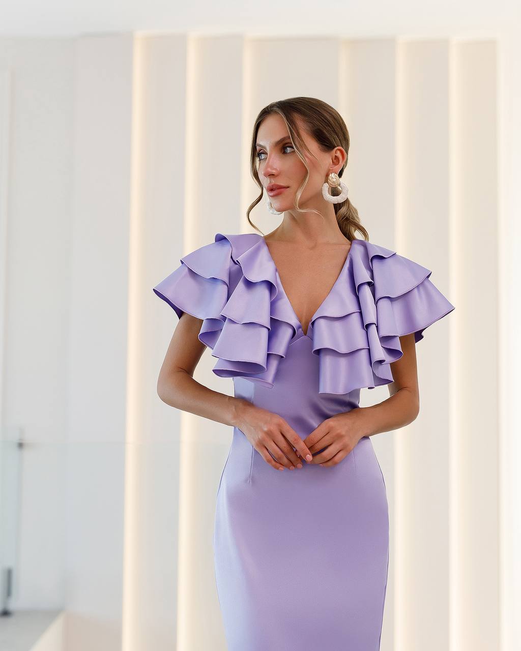Woman wearing a lavender dress with ruffled shoulders against a neutral background