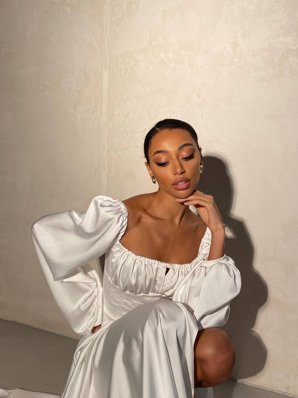 Woman in a white dress sitting against a plain background