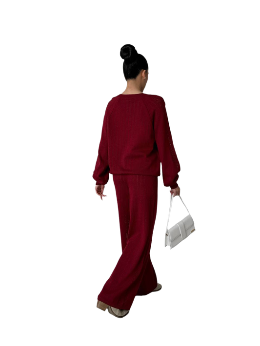 Person wearing a burgundy outfit holding a white clutch on a white background