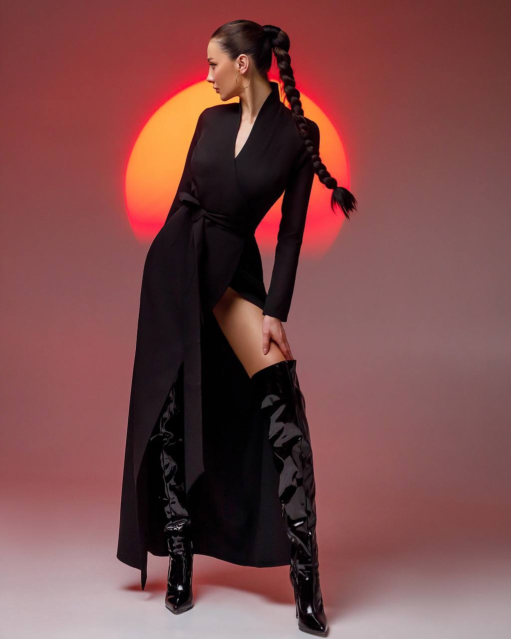 Woman in a black outfit with high boots against a red and orange background