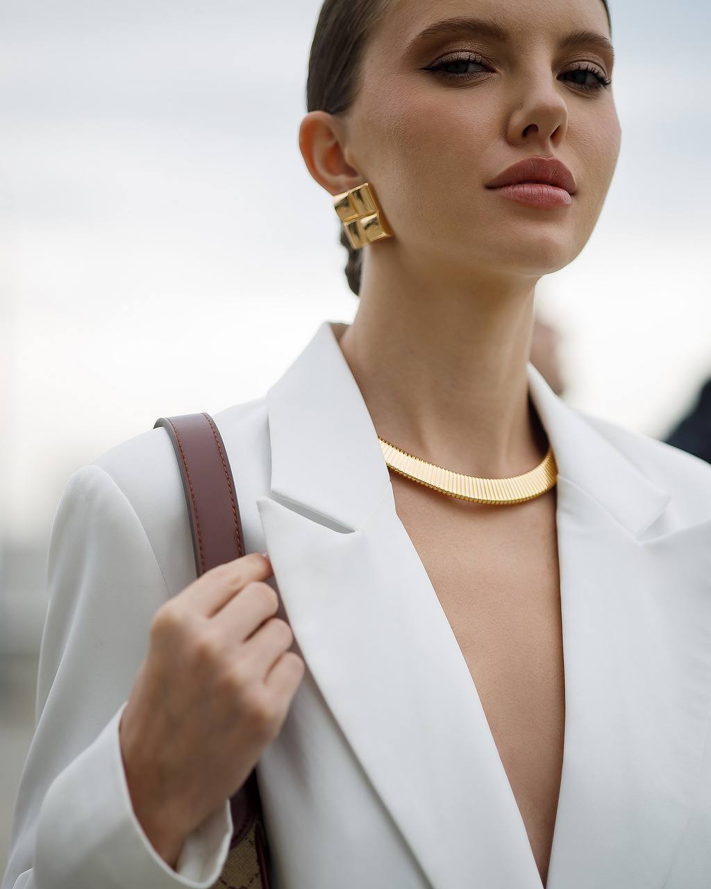 Woman wearing a gold necklace and earrings with a blurred background