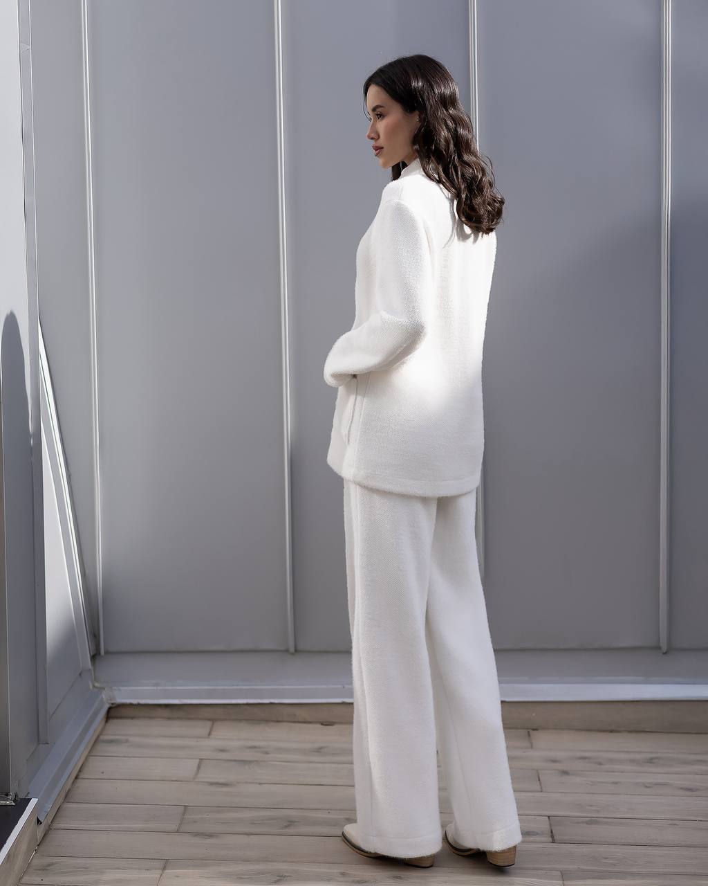 Woman wearing a white outfit standing in a room with gray walls and wooden floor.