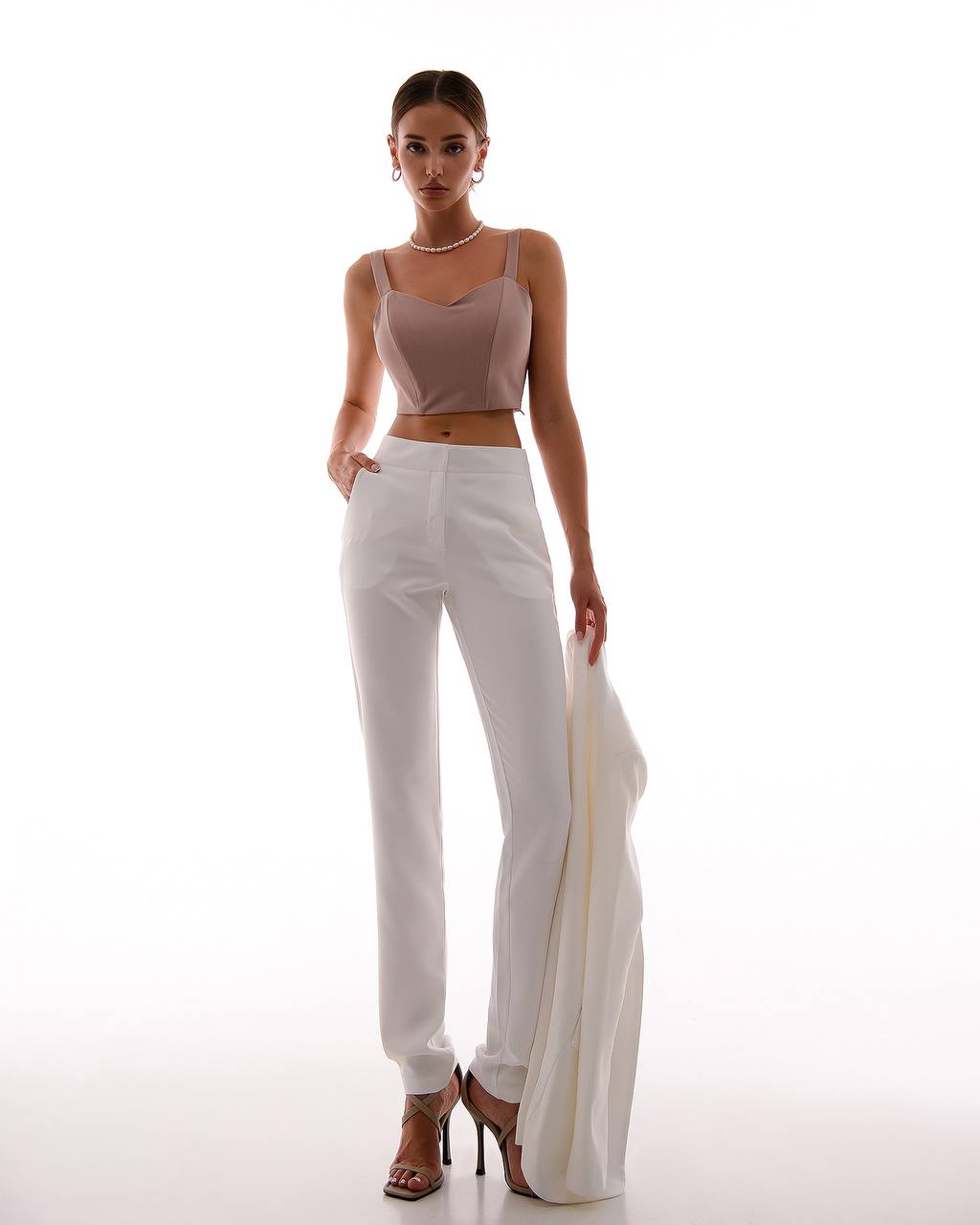 Woman wearing a beige top and white pants on a white background