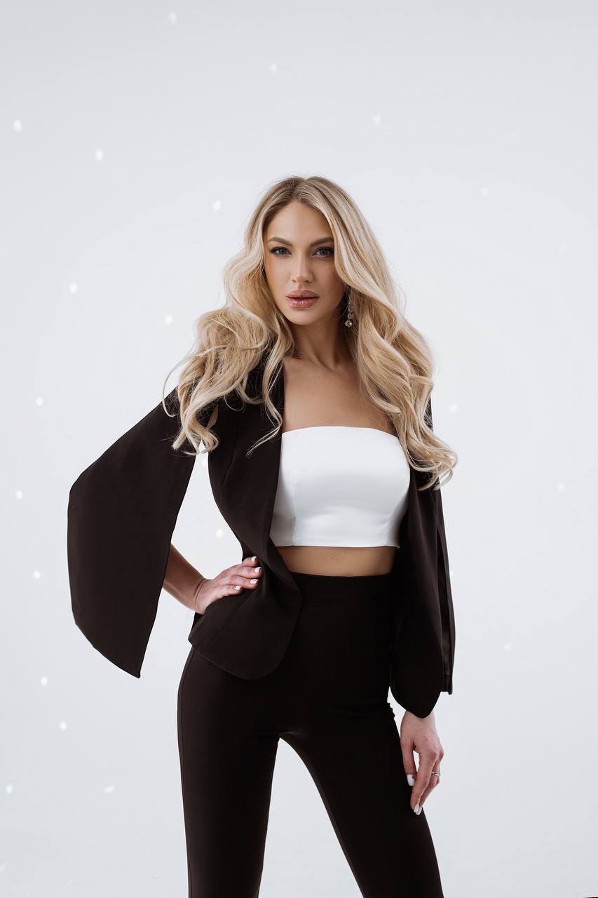 Woman wearing a black blazer over a white top and black pants on a light gray background