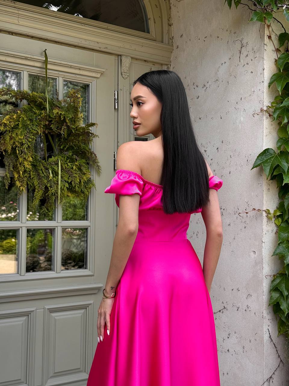 Woman in a bright pink dress standing in front of a door with plants.