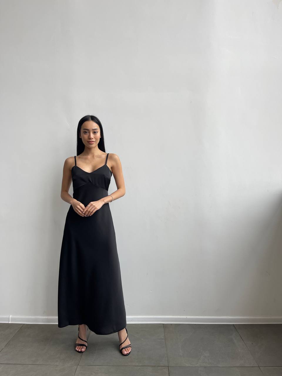 Woman wearing a black dress standing against a plain white wall.