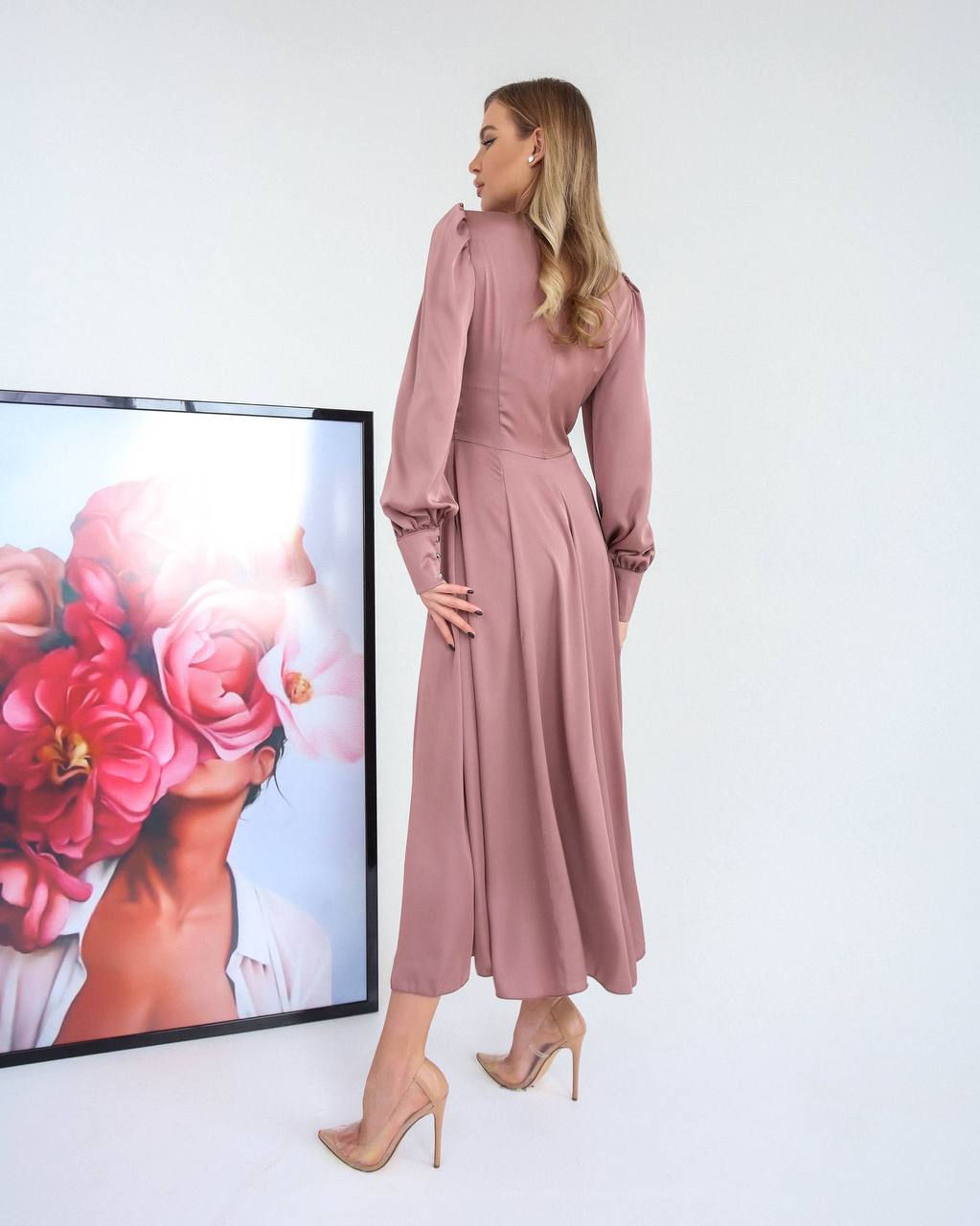 Woman in a pink dress standing in front of a floral painting on a white wall.