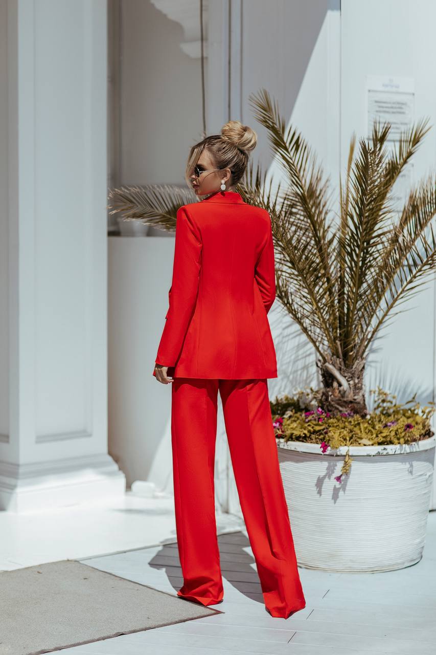 Person wearing a red suit standing in front of a white building with plants.