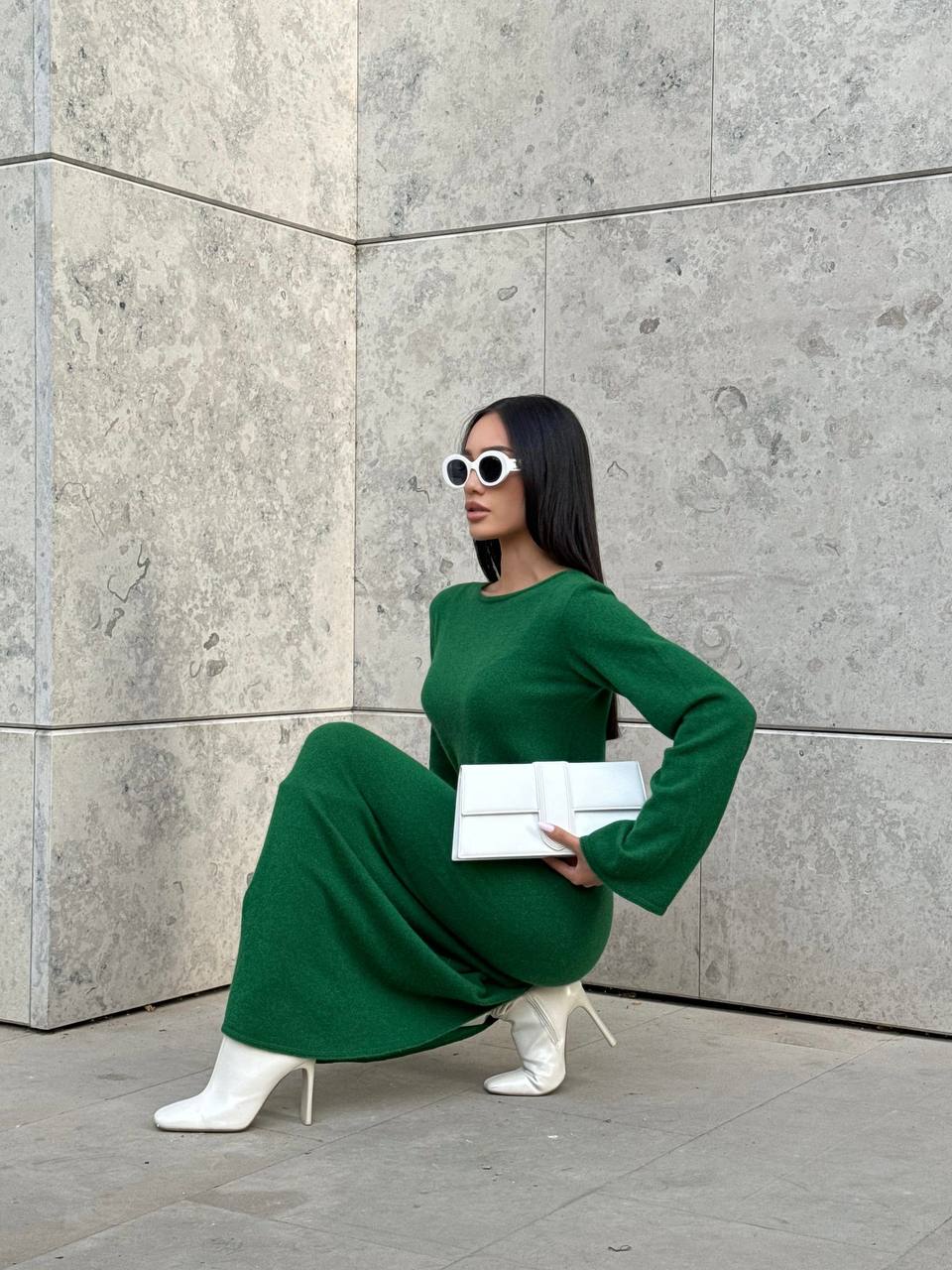 Woman in a green dress posing against a gray wall