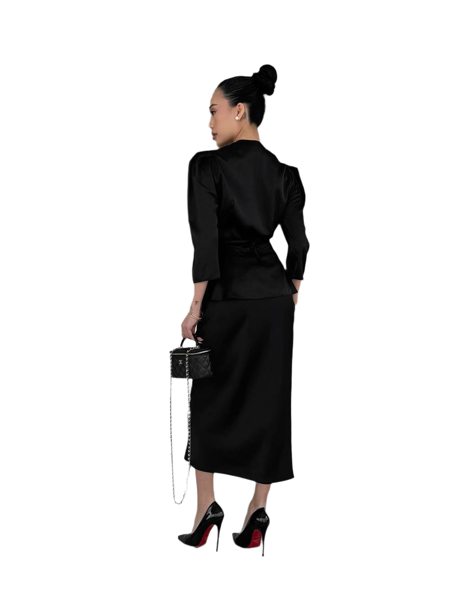 Woman wearing a black outfit with a skirt and top, holding a handbag on a white background