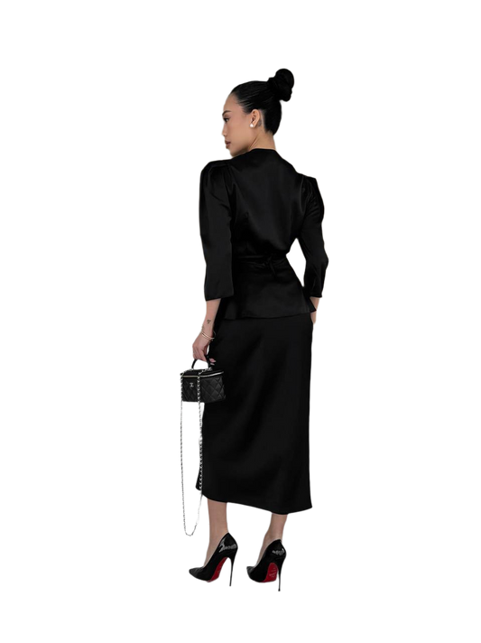 Woman wearing a black outfit with a skirt and top, holding a handbag on a white background