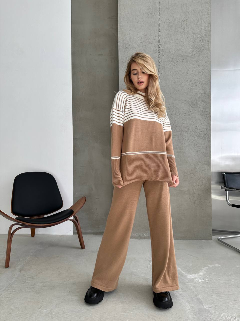 Woman wearing a brown and white striped sweater with matching pants in a minimalistic room.