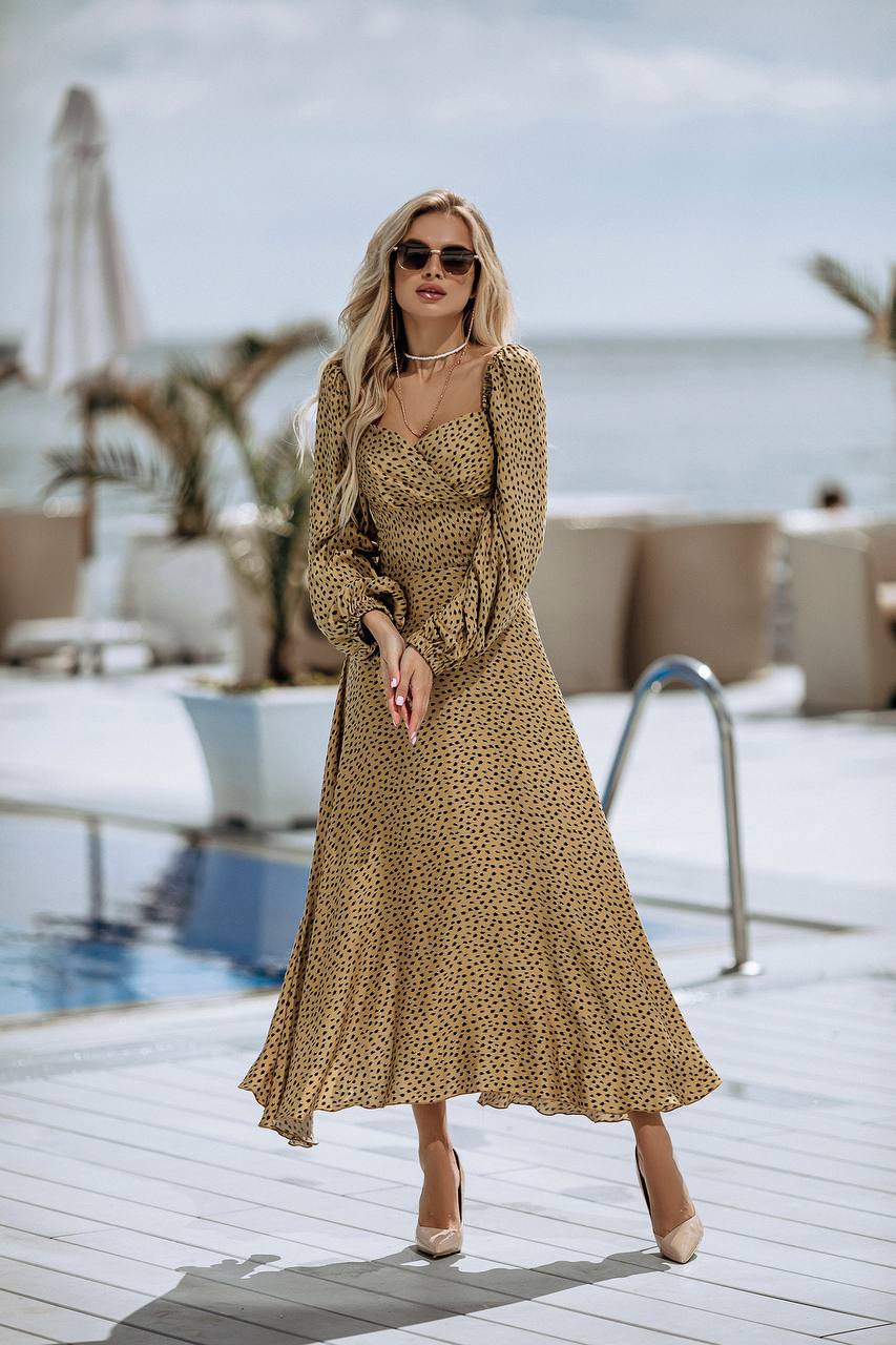 Woman in a gold polka dot dress standing by a poolside.