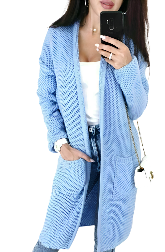 Person wearing a light blue cardigan with a white top and jeans, holding a phone.