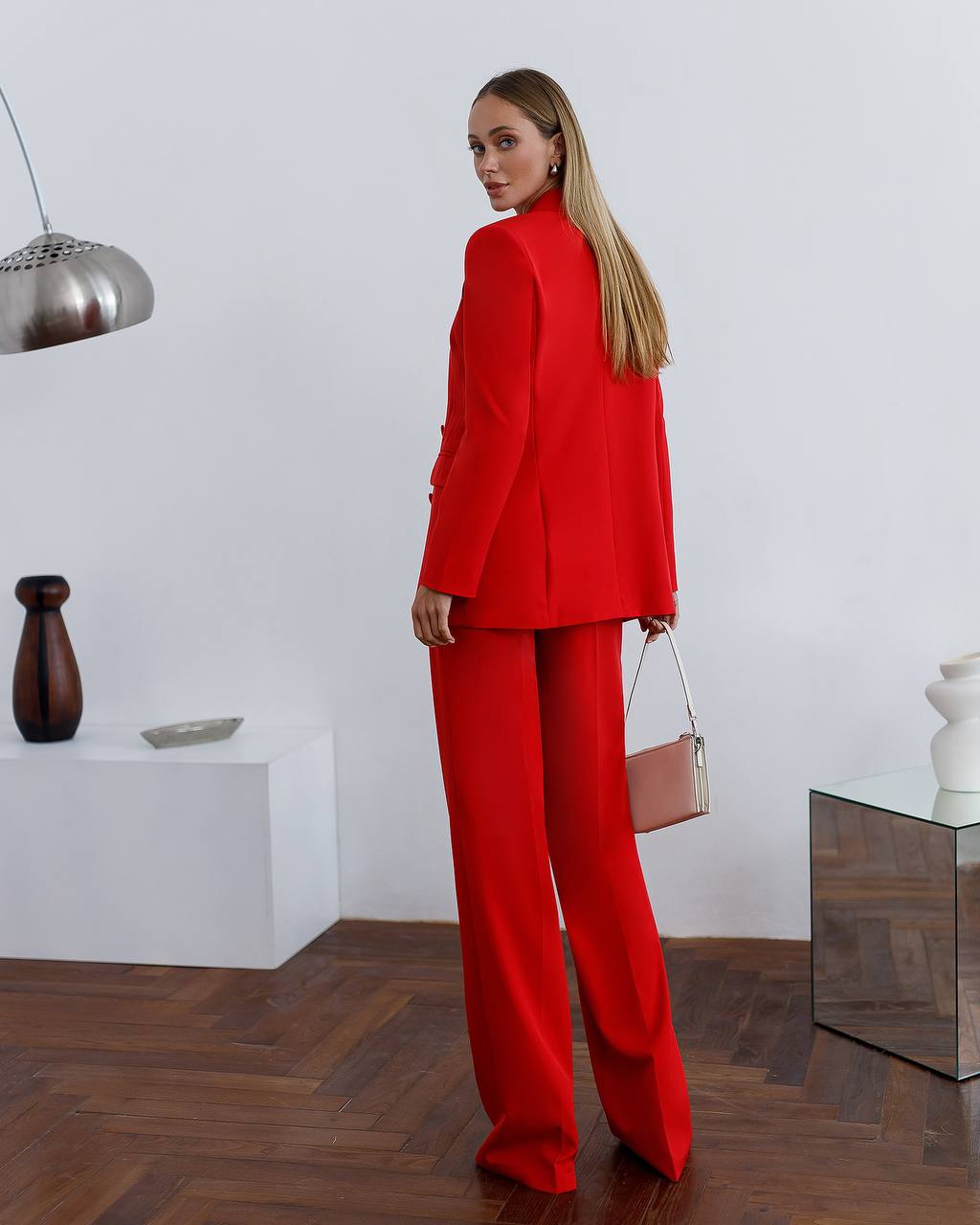 Woman in a red suit standing in a modern room with minimal decor.