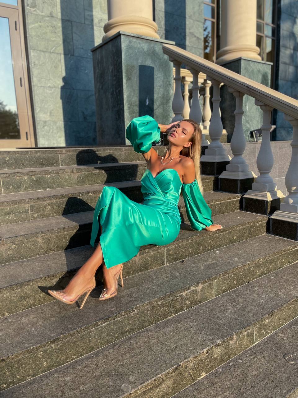 Woman in a green dress sitting on steps with classical architecture in the background