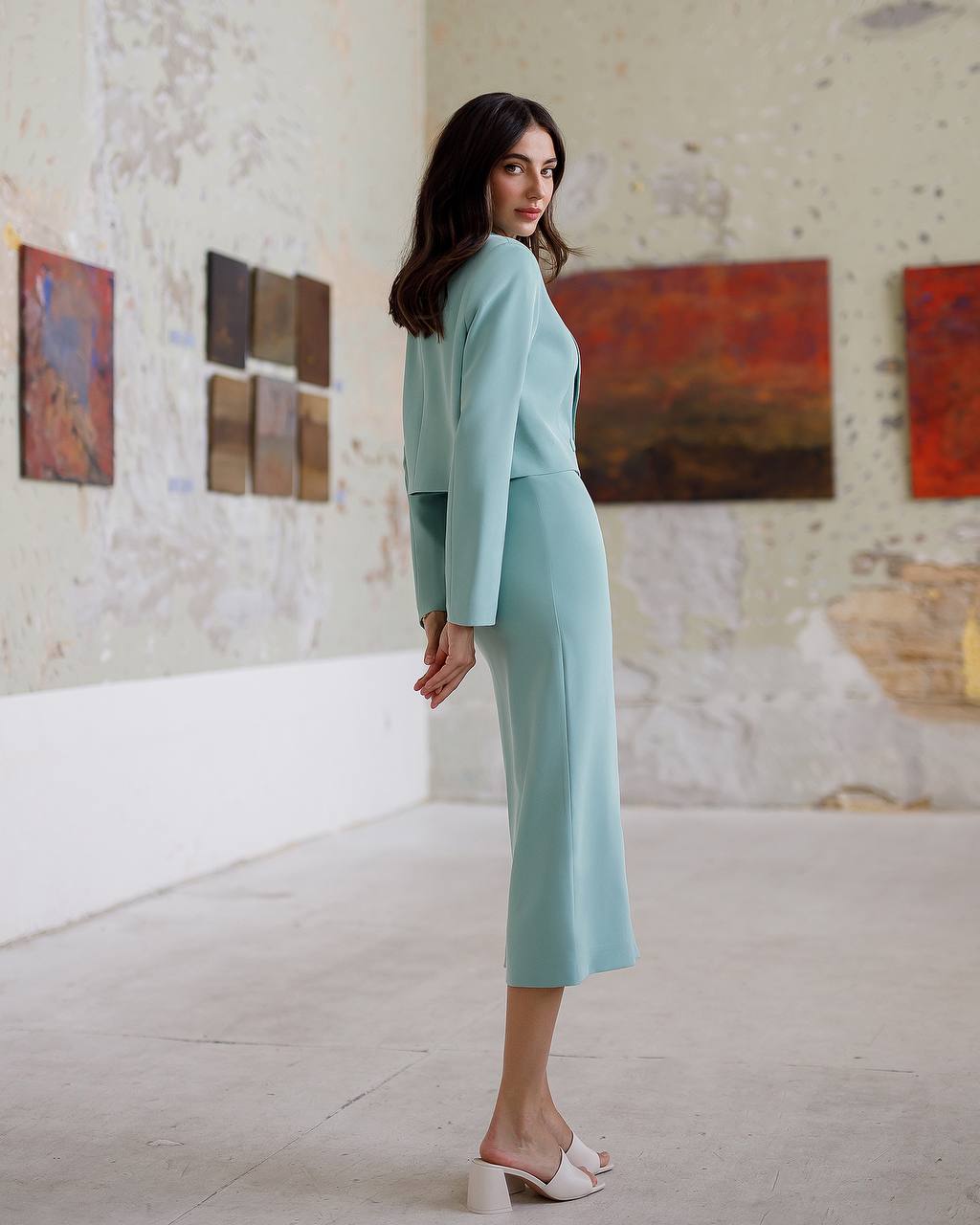 Woman in a light blue outfit standing in an art gallery with colorful paintings on the wall.