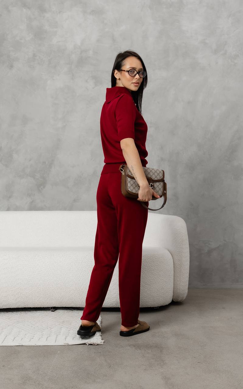 Woman in a red outfit holding a patterned handbag against a gray background