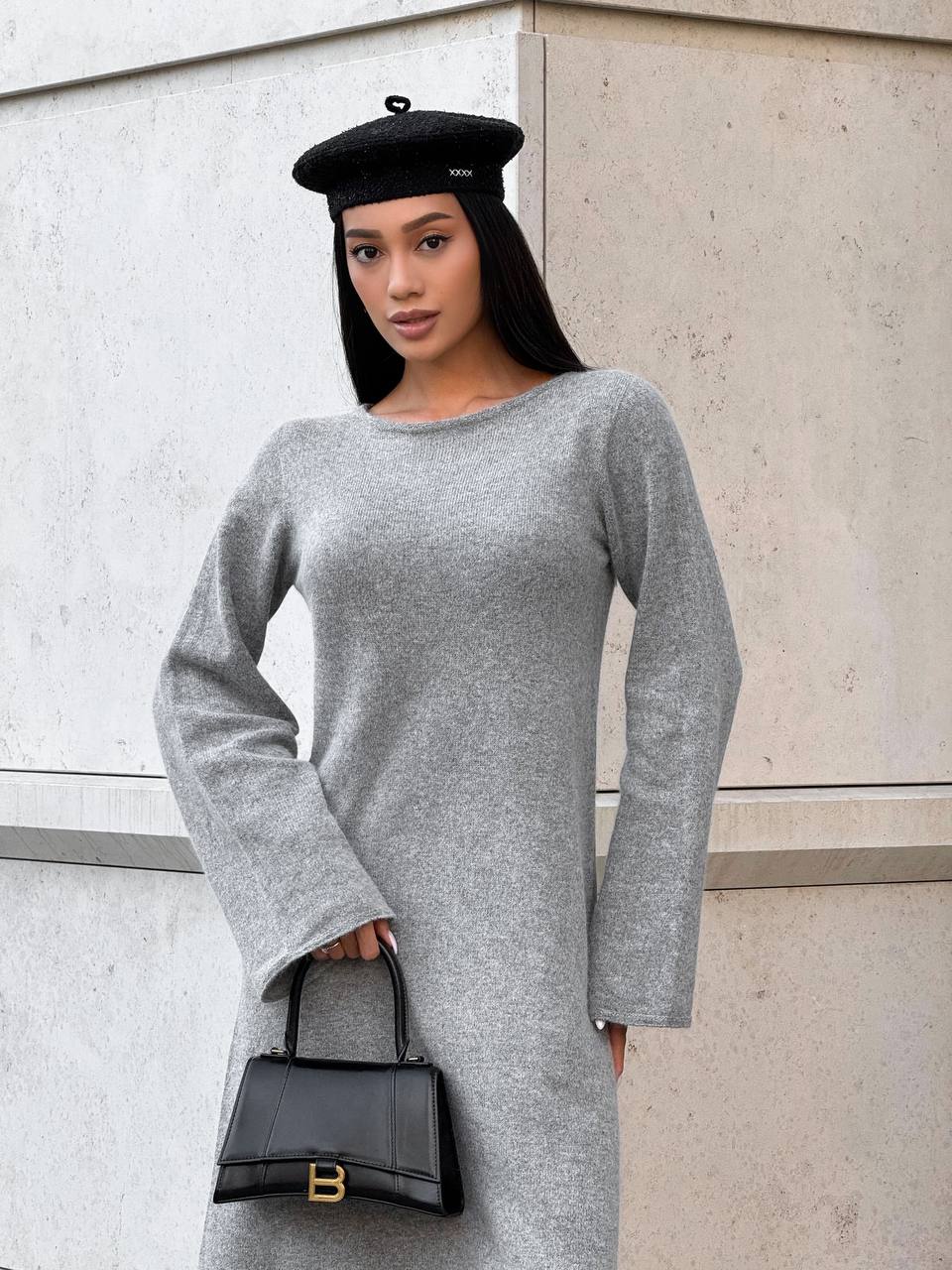 Woman wearing a gray sweater dress and black beret against a light-colored wall.