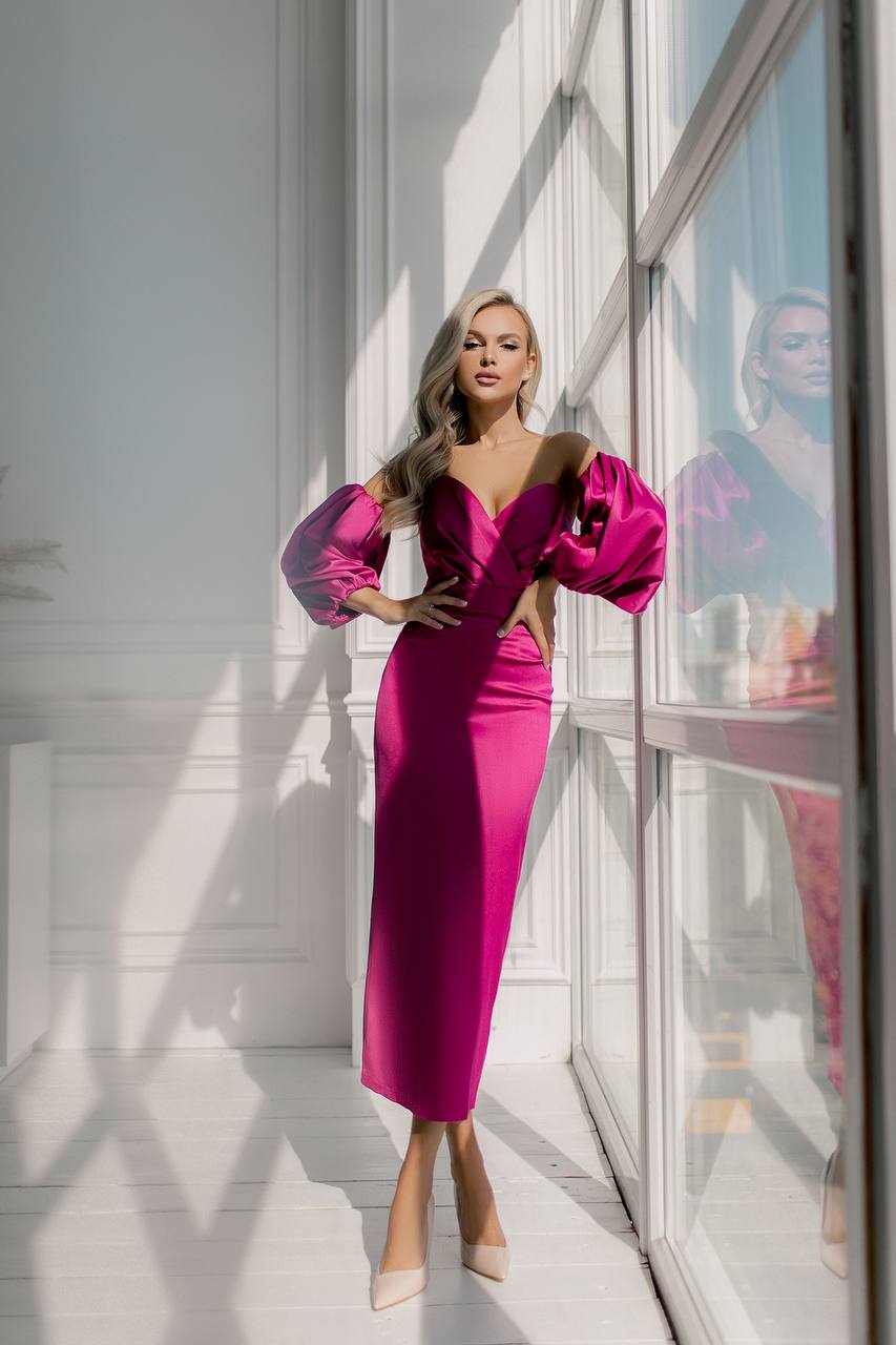 Woman in a bright pink dress with brown fur collar standing in a modern interior setting.