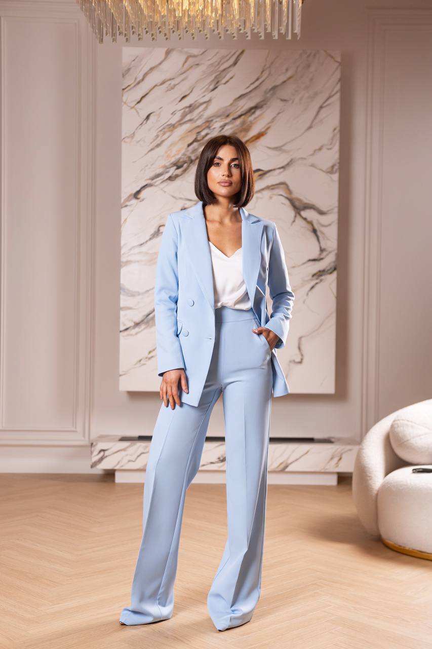 Woman in a light blue suit standing in a stylish room with marble wall art.