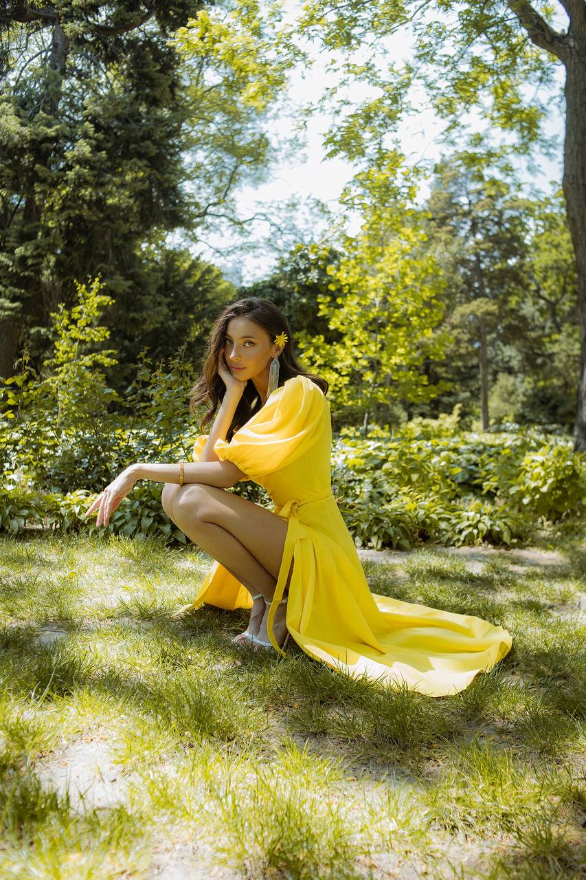 Woman in a yellow dress sitting in a park with greenery around