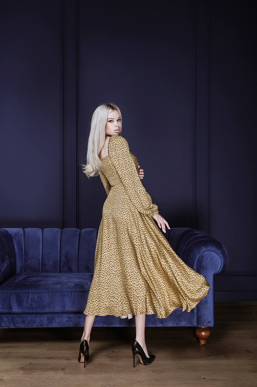 Woman in a gold dress standing in a room with a blue couch and dark walls.