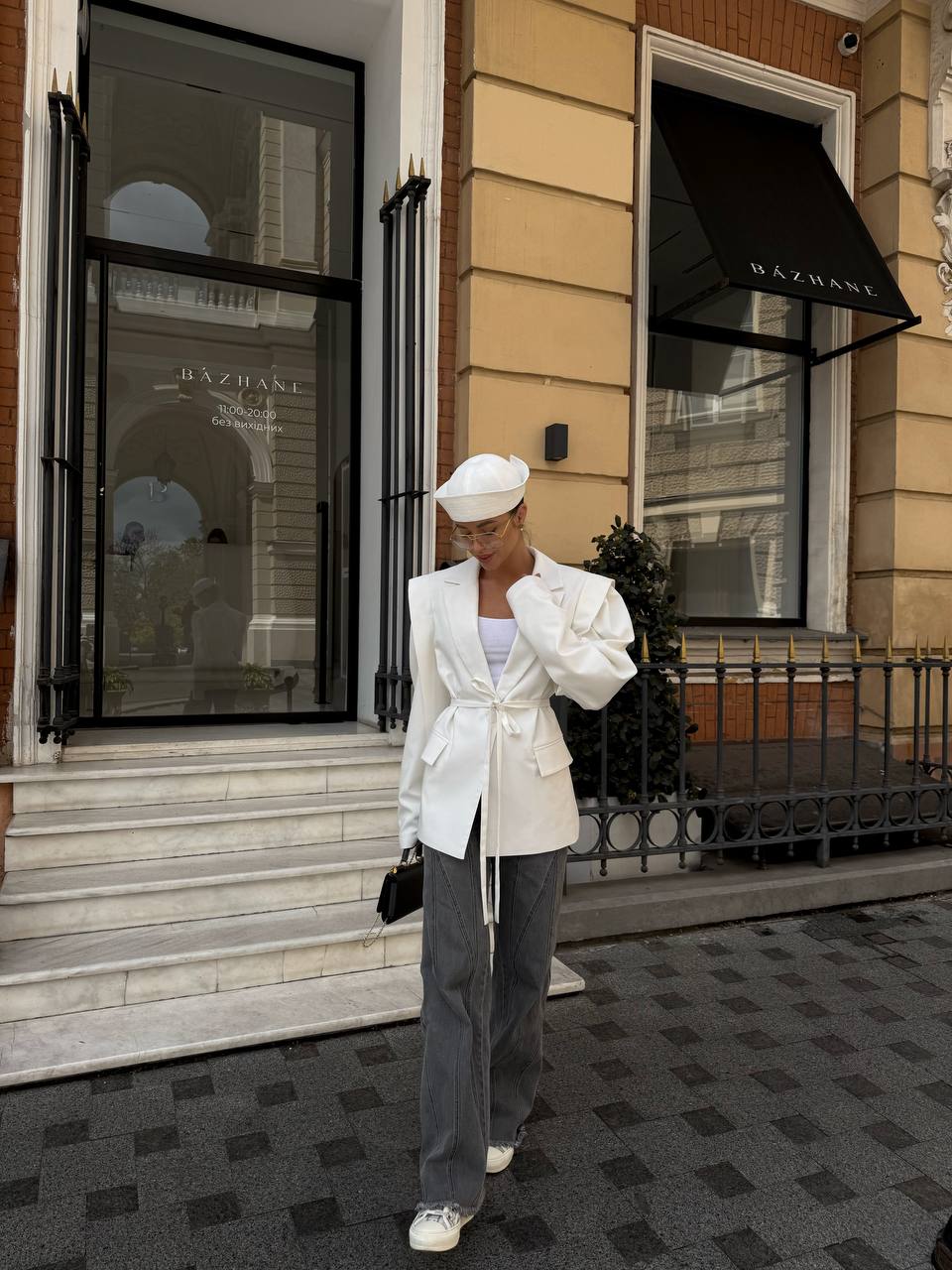 Person wearing a white outfit standing in front of a building with 'Dazhane' branding.