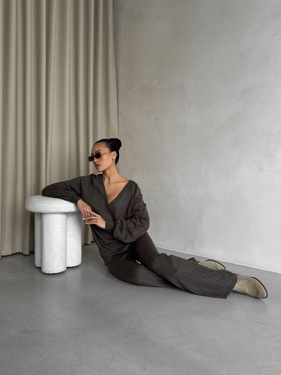 Person sitting on the floor against a neutral wall with a curtain.