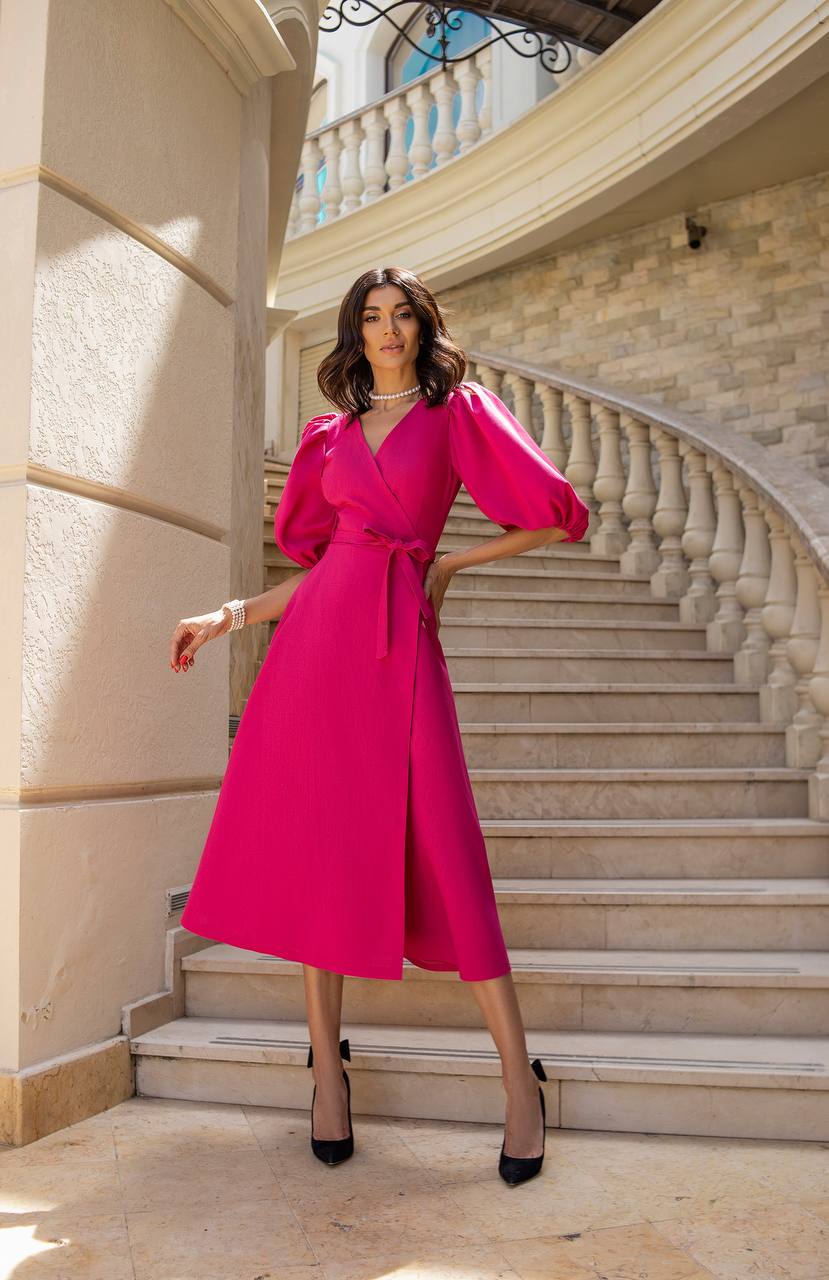 Woman in a bright pink dress standing on a staircase in an elegant building.