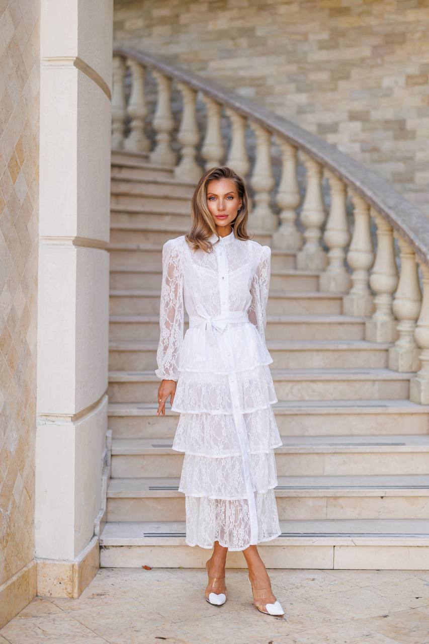 Woman in a white lace dress standing on stone steps with a neutral wall background